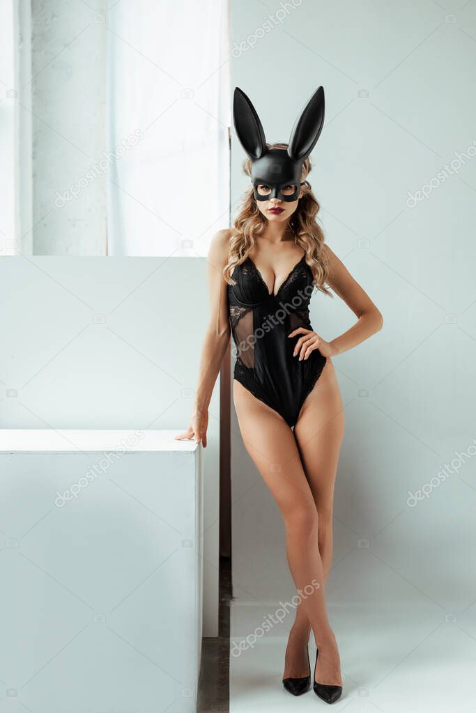 Seductive woman in bunny mask and bodysuit looking at camera on white background 