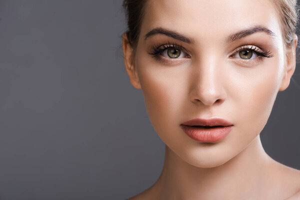 beautiful young woman with makeup looking at camera isolated on grey