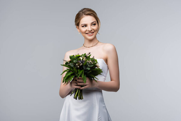 happy bride in white dress holding wedding flowers isolated on grey 