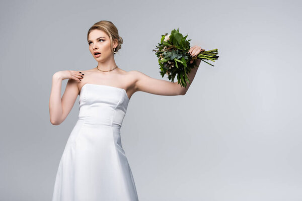 dissatisfied bride in white dress holding bouquet of flowers isolated on grey 