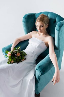 Beyaz koltukta otururken elinde çiçeklerle zarif gelinlik içinde güzel bir gelin.