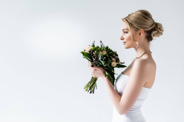 side view of attractive bride holding wedding flowers on white 