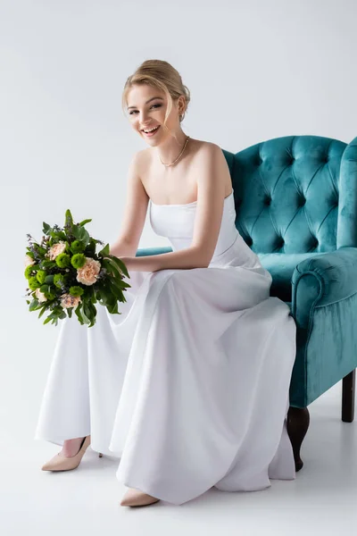Веселая Невеста Элегантном Свадебном Платье Цветами Сидя Кресле Белом — стоковое фото