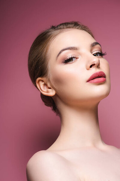 low angle view of nude and pretty woman with makeup looking at camera on pink 