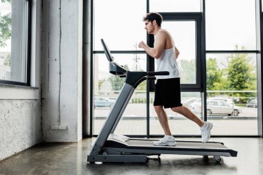 Spor salonunda koşu bandında koşan yakışıklı sporcunun yan görünüşü 