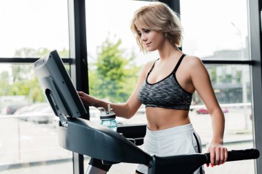 attractive sportswoman touching screen on modern treadmill  clipart