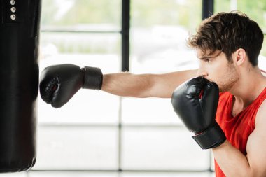 Boks eldivenli atletik sporcunun kum torbasıyla çalışmasının yan görünüşü 