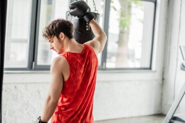 Spor giyimli yorgun adam ve boks eldivenleri kum torbasına dokunuyor. 