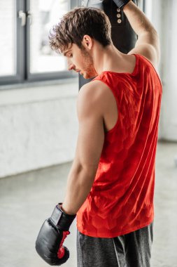Spor kıyafetleri ve boks eldivenleri giymiş yorgun bir adam kum torbasına dokunuyor. 