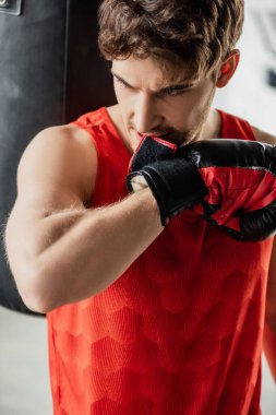 Spor giyimli sporcu spor salonunda boks eldiveni ısırıyor. 