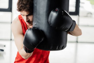 Spor giyimli yorgun bir adam ve spor salonunda kum torbasına dokunan siyah boks eldivenleri. 
