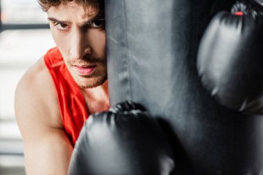 Spor kıyafetleri içinde yorgun bir adam ve spor salonunda kum torbasına dokunan siyah boks eldivenleri. 