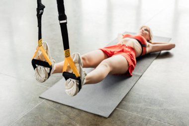Spor kıyafetleri içinde sportif genç bir bayanın seçici odak noktası. Kondisyon minderinde yatarken direnç bantlarıyla egzersiz yapıyor. 