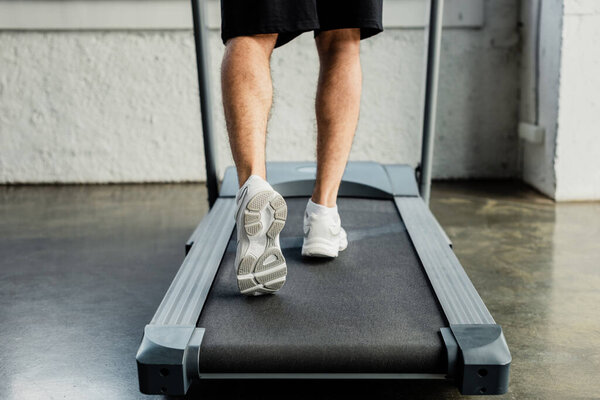 cropped view of sportsman running on treadmill in gym 