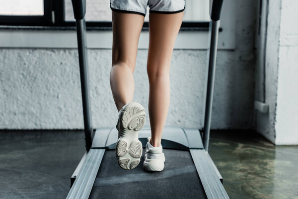 cropped view of sportswoman running on treadmill in gym 