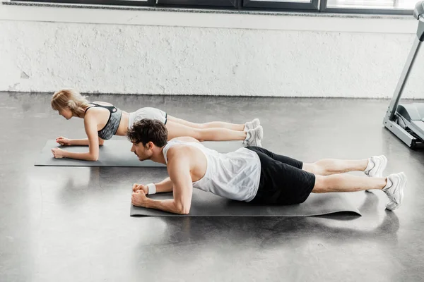 side view of sports couple doing plank on fitness mats in gym