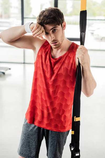 exhausted sportsman standing and touching resistance bands in gym