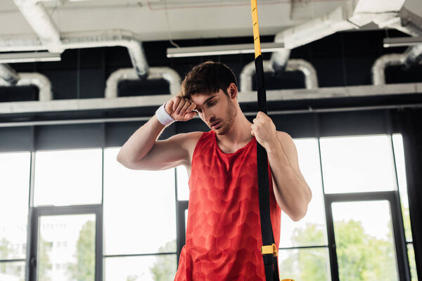 exhausted and sweaty sportsman standing and touching face near resistance bands in gym 