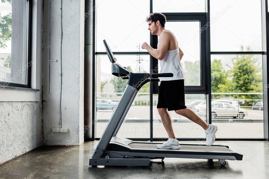 side view of handsome sportsman running on treadmill in gym 