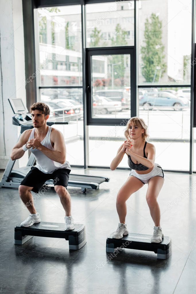 sportsman and sportswoman with clenched hands exercising near step platforms 