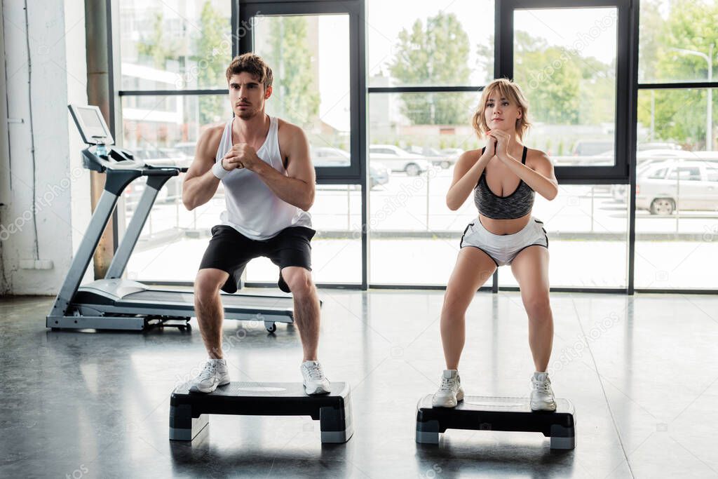 handsome sportsman and attractive sportswoman with clenched hands exercising on step platforms 