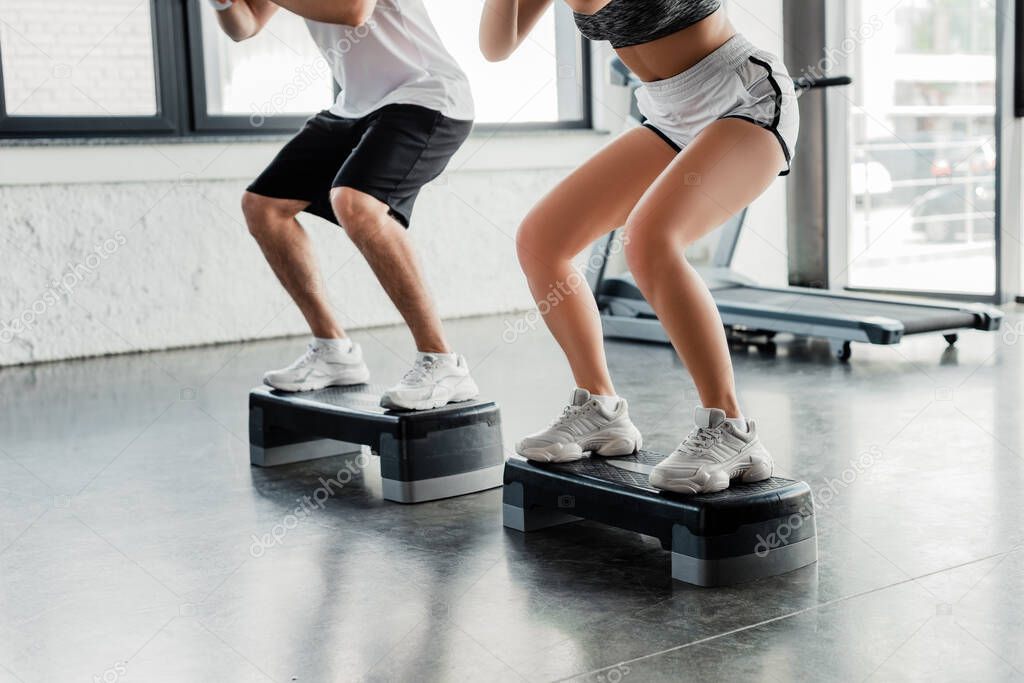 cropped view of sportsman and sportswoman exercising on step platforms 