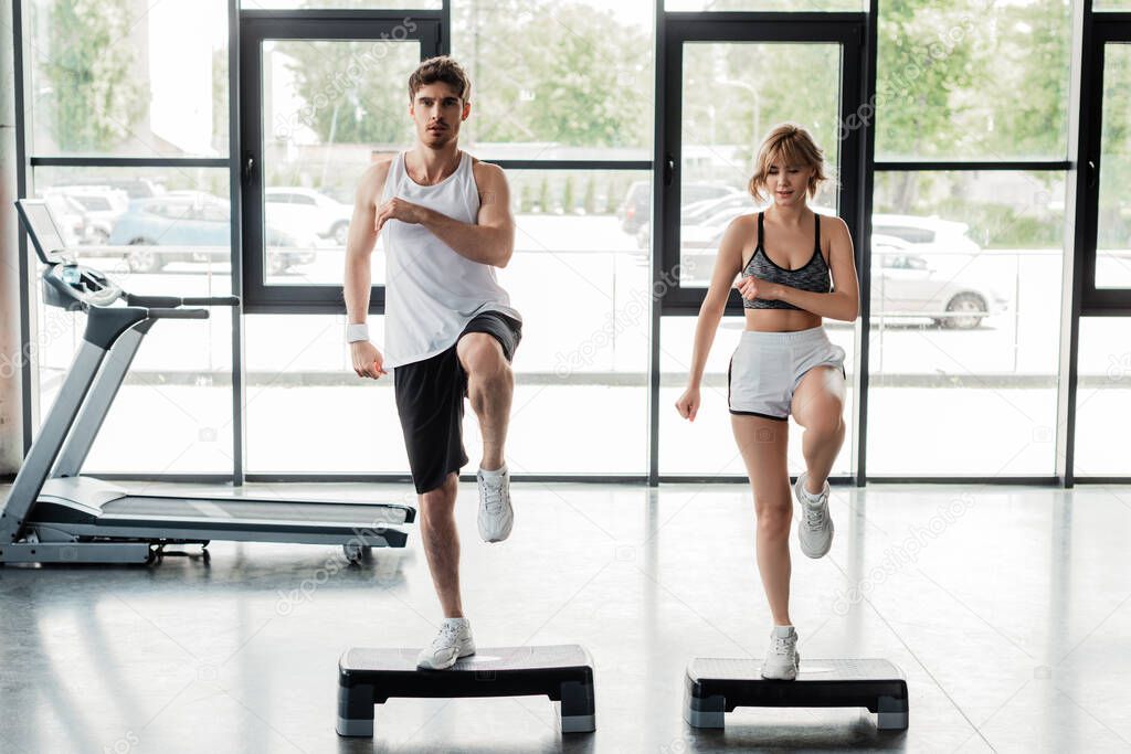 handsome sportsman and attractive sportswoman exercising on step platforms 