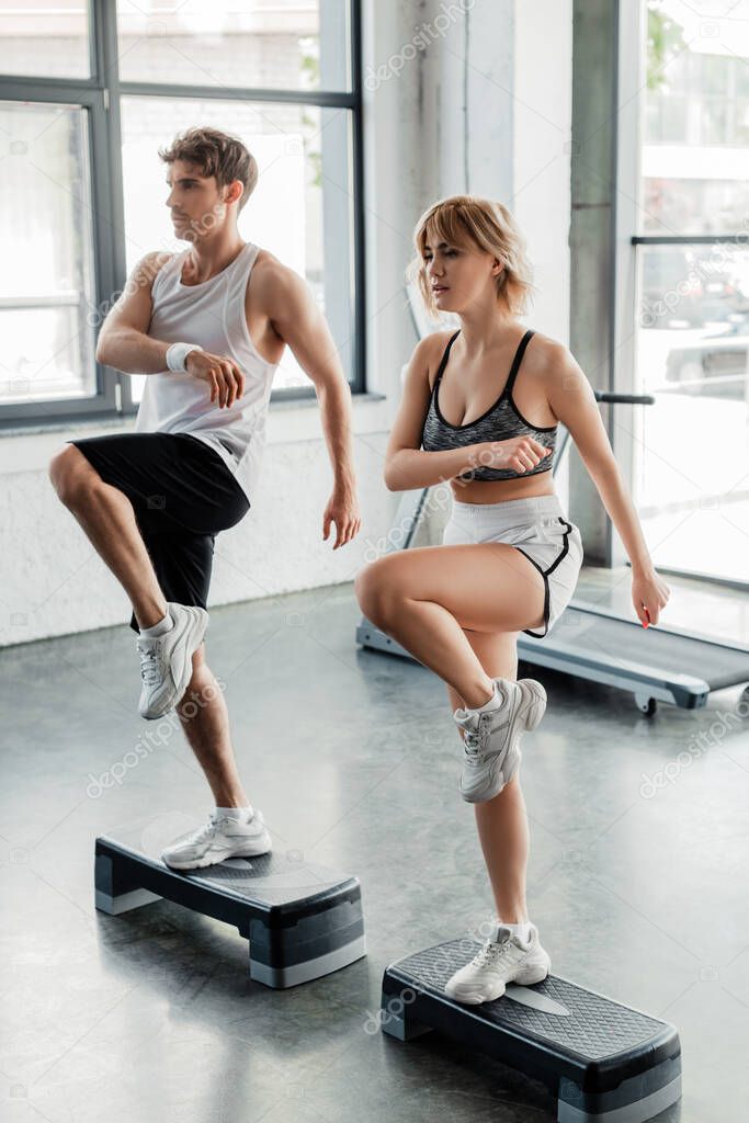 selective focus of young sport couple exercising on step platforms in gym