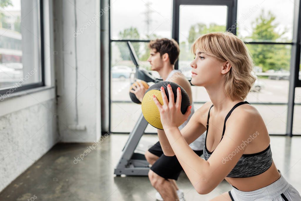 selective focus of attractive sportswoman exercising with ball near sportive man 
