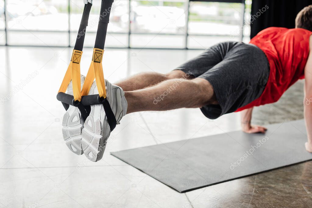 cropped view of athletic man in sportswear exercising with resistance bands on fitness mat 