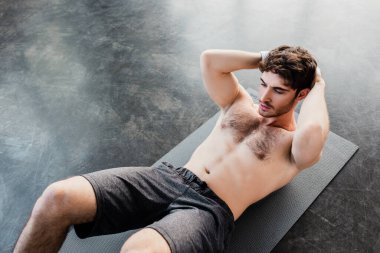 Yüksek açılı, yakışıklı sporcunun spor salonundaki spor minderinde mekik çekişi. 