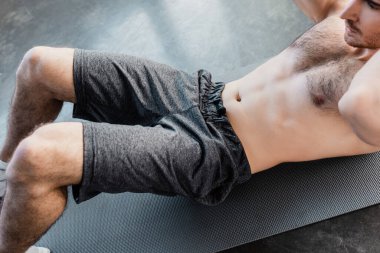 Üstsüz sporcunun spor salonundaki spor minderinde mekik çekişini. 