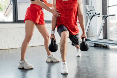 Spor salonundaki ağır dambıllarla spor yapan sporcu bir kadının kesikli görüntüsü. 