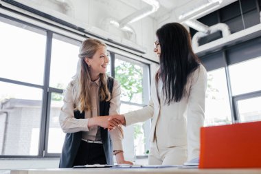Ofiste gülümseyen ve tokalaşan çekici iş kadınlarının seçici odağı 