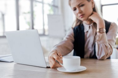 İş kadınının laptopun yanındaki kahveye dokunduğu seçici odak noktası 
