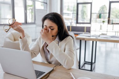 Kulaklık takmış yorgun operatör laptopun yanındaki gözlere dokunuyor 