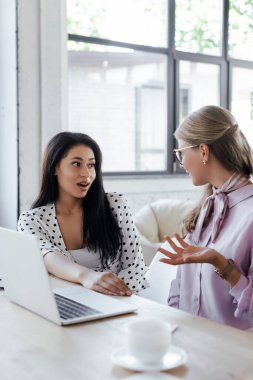 Modern ofiste dizüstü bilgisayarın yanında dedikodu yapan iş kadınlarının seçici odak noktası