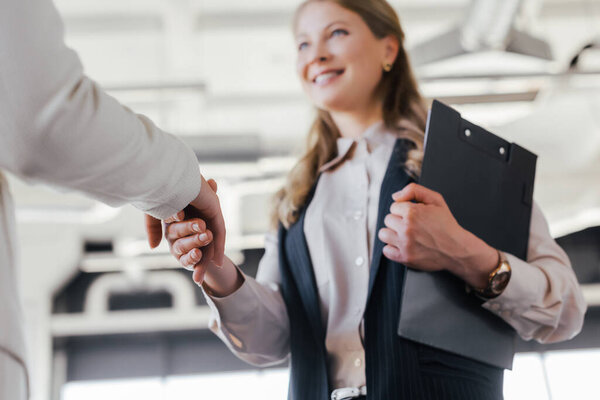 selective focus of smiling businesswoman shaking hands with coworker in office