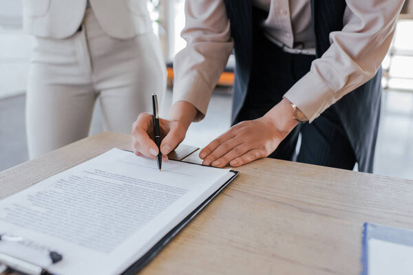 cropped view of businesswoman signing contract near coworker 