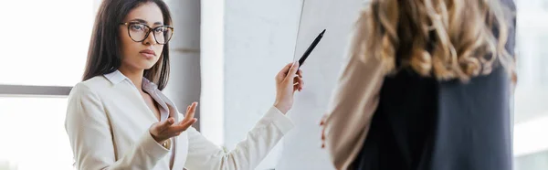 Tiro Panorâmico Empresária Óculos Segurando Caneta Marcador Perto Flipchart Olhando — Fotografia de Stock