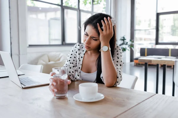 办公室里 头痛的女人在一杯咖啡和笔记本电脑前拿着一杯水 — 图库照片