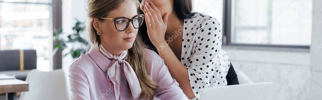 website header of businesswoman whispering in ear of coworker in glasses while gossiping in office 