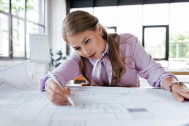 selective focus of attractive businesswoman drawing blueprints in office clipart