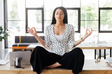 Güzel bir iş kadını. Gözleri kapalı. Masada meditasyon yapıyor.