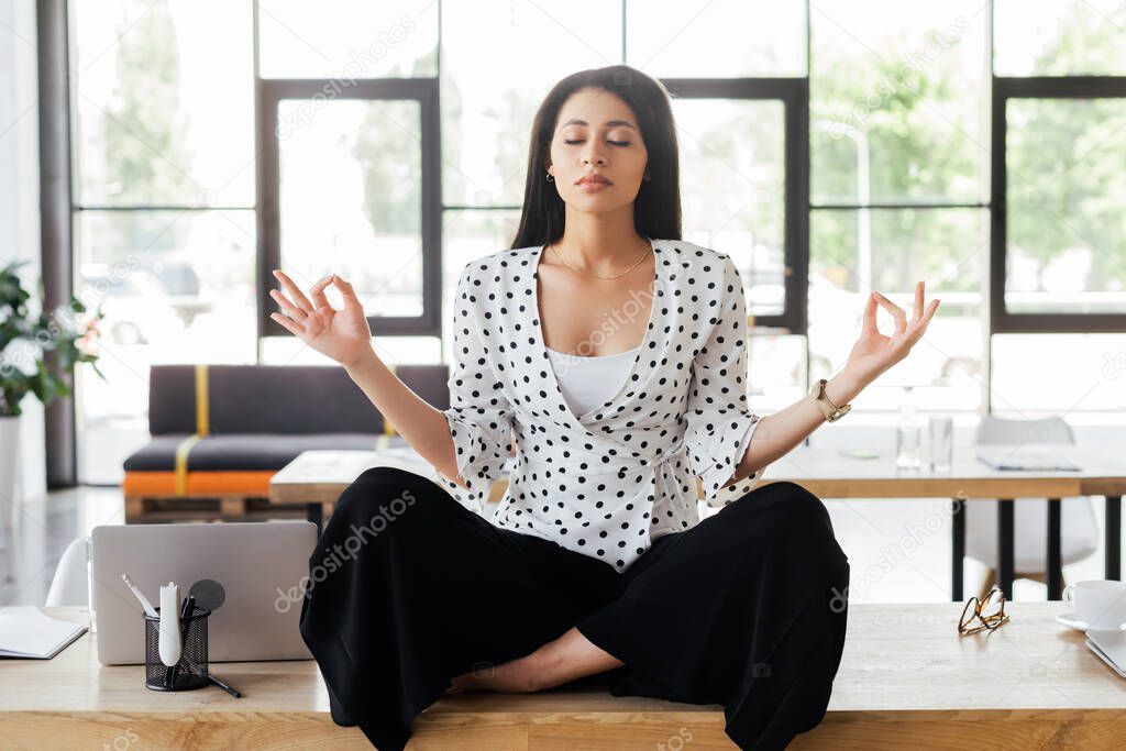 beautiful businesswoman with closed eyes meditating on table in office