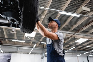 low angle view of technician touching car tire in service station  clipart