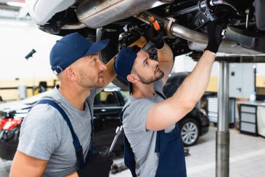 Yakından el feneri tutan şapkalı yakışıklı bir tamirci ve benzin istasyonunda çalışan bir araba. 