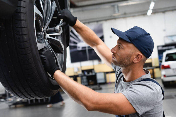 боковой вид техники в резиновых перчатках, касающихся колесных дисков при ремонте автомобиля