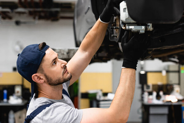 side view of mechanic in cap and rubber gloves fixing vehicle 