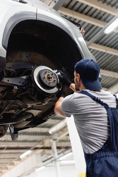low angle view of mechanic in rubber gloves touching car brake and fixing vehicle 
